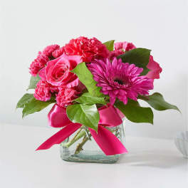 Pink flowers arranged in a clear glass vase with a satin ribbon