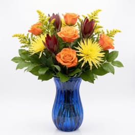 Orange roses and yellow spider mums in a blue glass vase