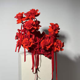 Red rose arrangement with long ribbon streamers on a white pedestal