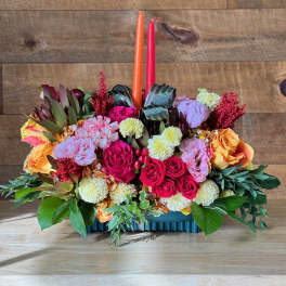 Colorful floral centerpiece with two taper candles in a low rectangular container