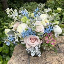 Mixed bouquet of pastel roses, white blooms, and blue flowers in a vase