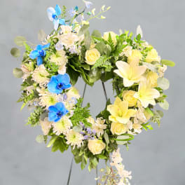 Heart-shaped floral wreath with yellow roses, white lilies, and blue orchids