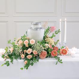 Peach and pink floral centerpiece around a silver urn with candles