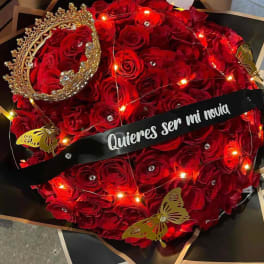 Red rose bouquet with a jeweled crown and a black ribbon reading "Quieres ser mi novia"