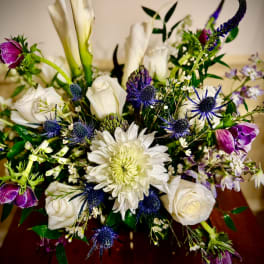 Mixed arrangement of white roses, calla lilies and purple and blue blooms in a vase