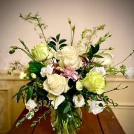 Arrangement of white and pale green roses with soft pink blooms in a clear glass vase on a wooden table