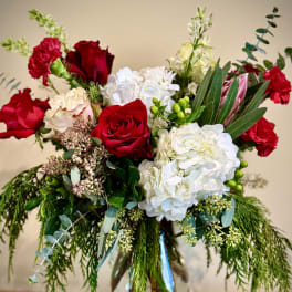 Tall arrangement of red roses, red carnations, white hydrangeas and evergreen foliage in a clear glass vase