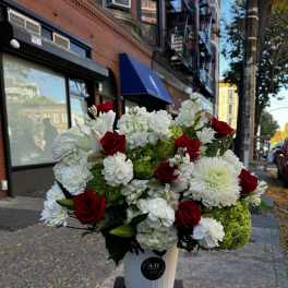 Red roses and white flowers arranged in a white bucket on a stand