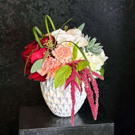 Asymmetrical mixed arrangement with red roses, peach carnations, white orchids, and succulents in a white ceramic vase