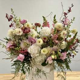 Large airy arrangement of white and pink flowers with burgundy accents in a tall white ceramic vase.