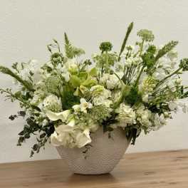 White and green flower arrangement in a textured white bowl on a wooden surface