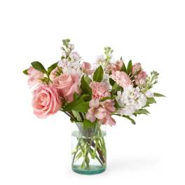 Pink roses, carnations, and white stock arranged in a clear glass cylinder vase