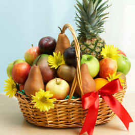 Wicker basket filled with assorted fresh fruit, yellow daisies, and a red ribbon bow