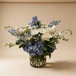 Blue and white arrangement with roses, mums, and hydrangeas in a clear glass cylinder vase