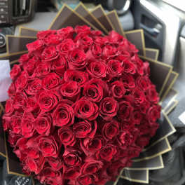 Large round bouquet of tightly packed red roses wrapped in layered black and gold paper.