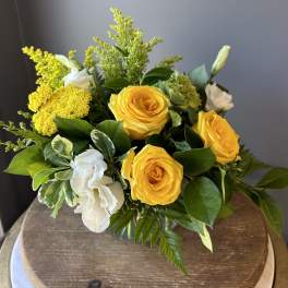 Compact arrangement of yellow roses with white blooms and fillers in a clear glass vase