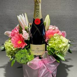 Champagne bottle in a pink floral gift arrangement with a ribbon