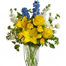 Yellow lilies and roses in a clear glass vase with blue and white flowers