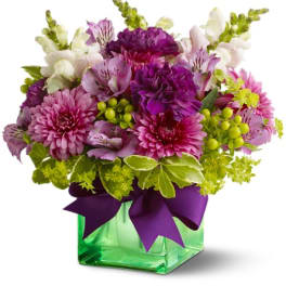 Purple and pink mixed bouquet in a green glass vase with a ribbon