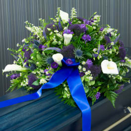 Purple and white funeral spray on a casket with a blue ribbon