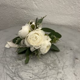 Small white ranunculus corsage with ribbon and foliage on a gray scratched surface