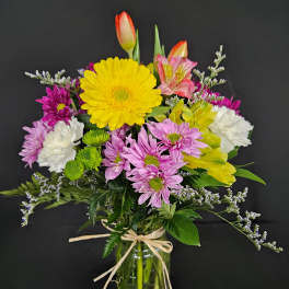 Mixed spring bouquet with yellow gerbera, tulips, carnations and daisies in a glass jar vase.
