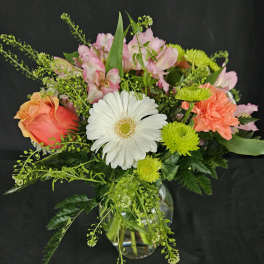 Mixed bouquet with white gerbera daisy, orange rose, pink blooms, and green mums in a clear glass vase.
