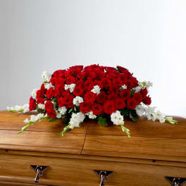 Red rose casket spray with white accent flowers resting on a wooden casket