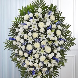 Tall standing spray of white lilies, roses and mums with blue flowers and palm fronds.