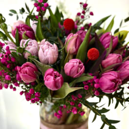 Pink tulips and magenta flowers arranged in a glass vase with a pink ribbon