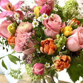 Mixed bouquet of pink roses, tulips, and daisies in a glass vase
