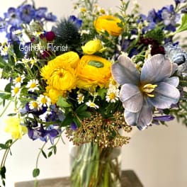 Mixed bouquet in a clear glass vase with yellow, blue, and white flowers