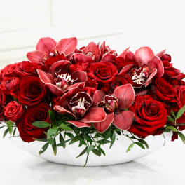 Red roses and orchids arranged in a white bowl vase