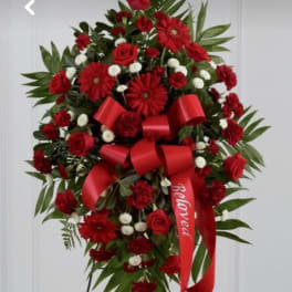 Tall red and white funeral spray on an easel with roses, daisies, and a red 'Beloved' ribbon