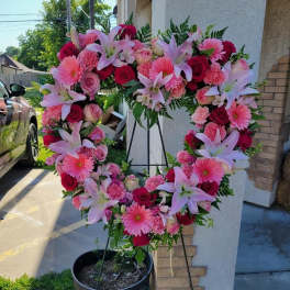 Large pink and red floral wreath on a stand with lilies and roses