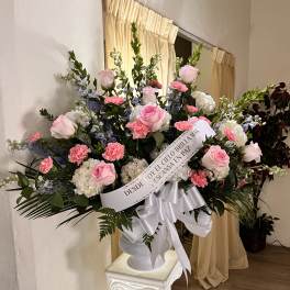 Tall pink and white sympathy arrangement in white urn with memorial ribbon on a pedestal