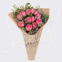 Cone-wrapped bouquet of pink roses with small pink filler flowers in kraft paper