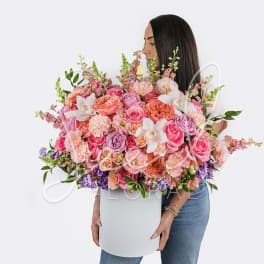 Large pink and peach flower arrangement in a white box held by a woman