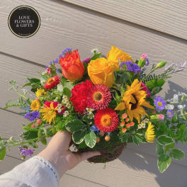 Bright mixed arrangement with yellow roses, red gerberas, and a sunflower in a low twig basket.