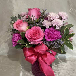 Pink roses and purple flowers in a magenta vase with a ribbon