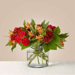 Low glass vase with red roses, orange alstroemeria, and red flowers arranged in a lush mixed bouquet