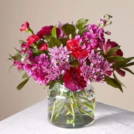 Pink and red mixed bouquet in a clear glass vase on a white table