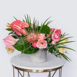 Pink tropical flower arrangement with ranunculus in a white ceramic vase on a marble table