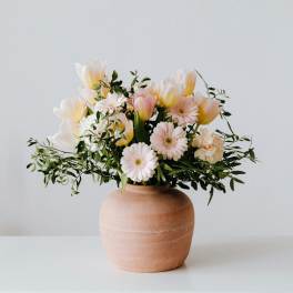 Pastel bouquet of tulips and daisies in a terracotta vase