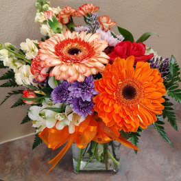 Mixed bouquet with orange gerberas and purple flowers in a glass vase