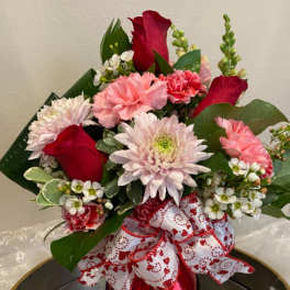 Bouquet of red roses, pink carnations, and pale chrysanthemums with a heart-patterned ribbon