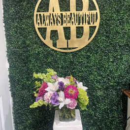 Mixed purple, pink, white, and green flowers in a glass vase on a pedestal.