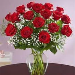 Arrangement of red roses with white filler flowers in a clear glass vase on a table