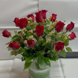 Red roses arranged in a clear glass vase with small white filler flowers