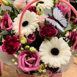 Pink and white mixed flower arrangement with gerbera daisies and carnations in a pink handled box with a butterfly decoration.